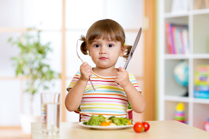 Una niña ante un plato de verduras.