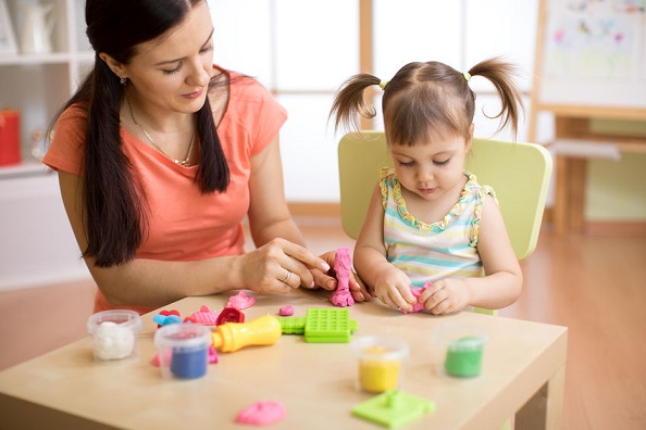 Una madre juega con su hija a hacer muñecos con platilina.