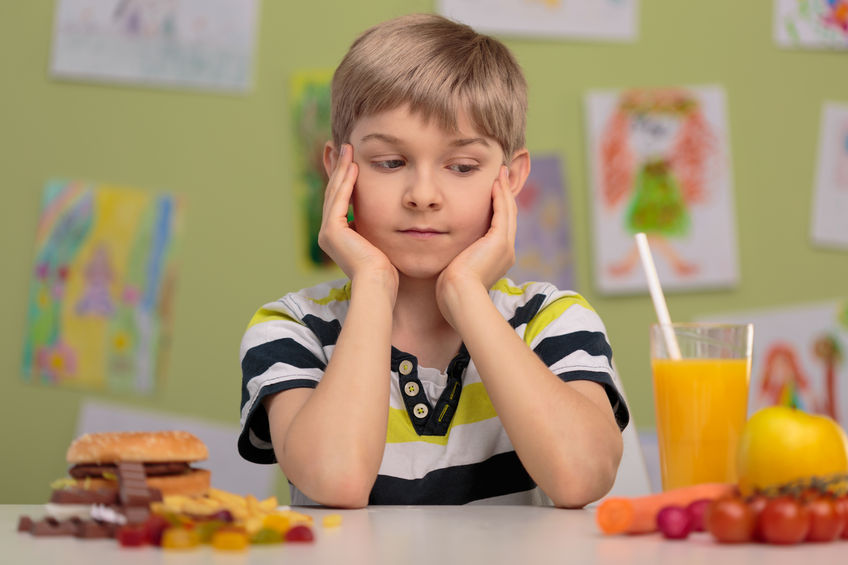 Niño duda entre comer un almuerzo saludable y otro rico en grasas