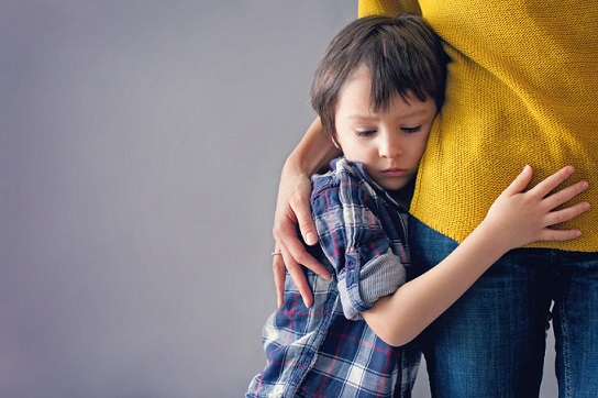 Un niño se agarra de su madre en una conducta infantil.