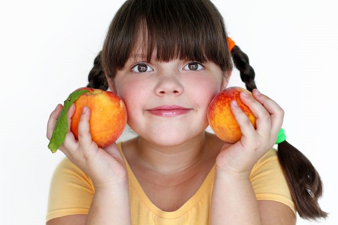 Una niña sostiene dos melocotones con sus manos.