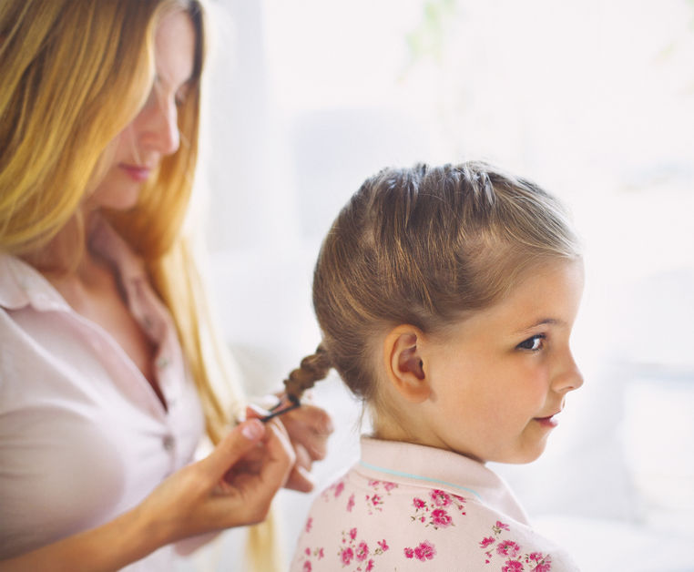 Madre que peina a su niña con trenzas