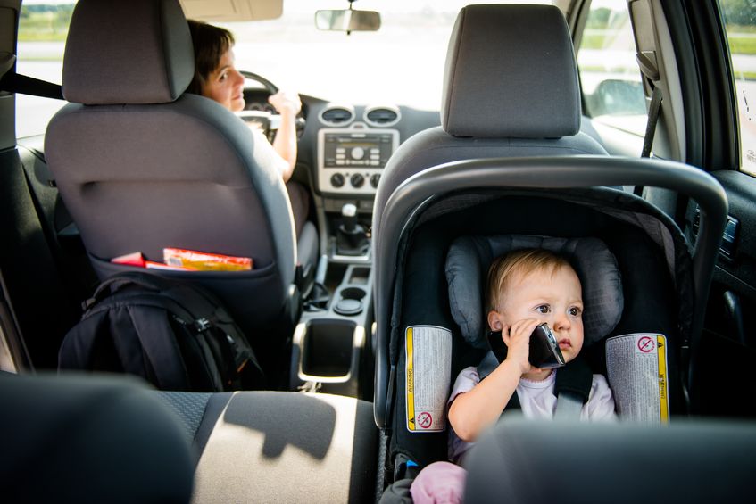 Niño pequeño sentado en su silla del coche jugando con el móvil