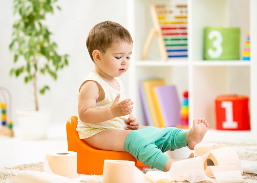 Niño sentado en orinal con rollos de papel higiénico