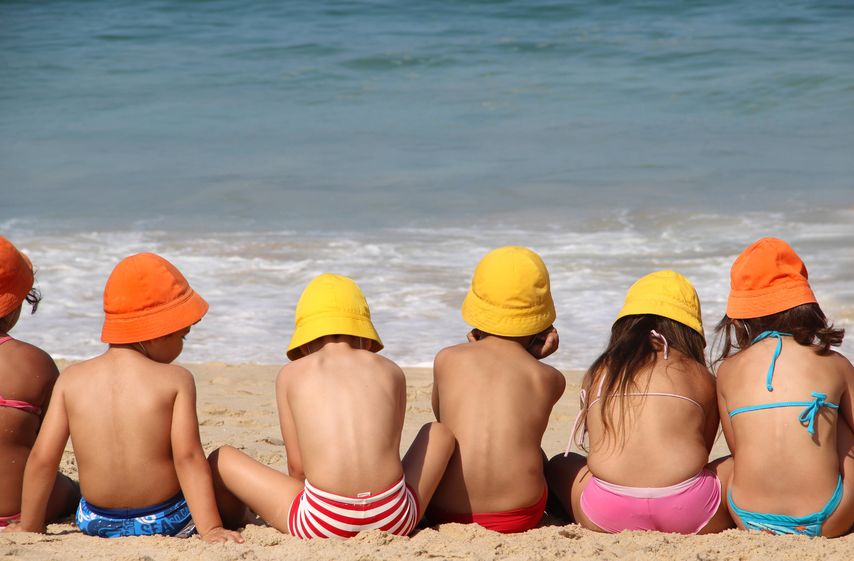 Niños con bañador y bikinis sentados en la arena de la playa