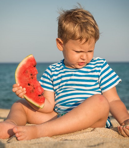 Un niño come un trozo de sandía en la playa.